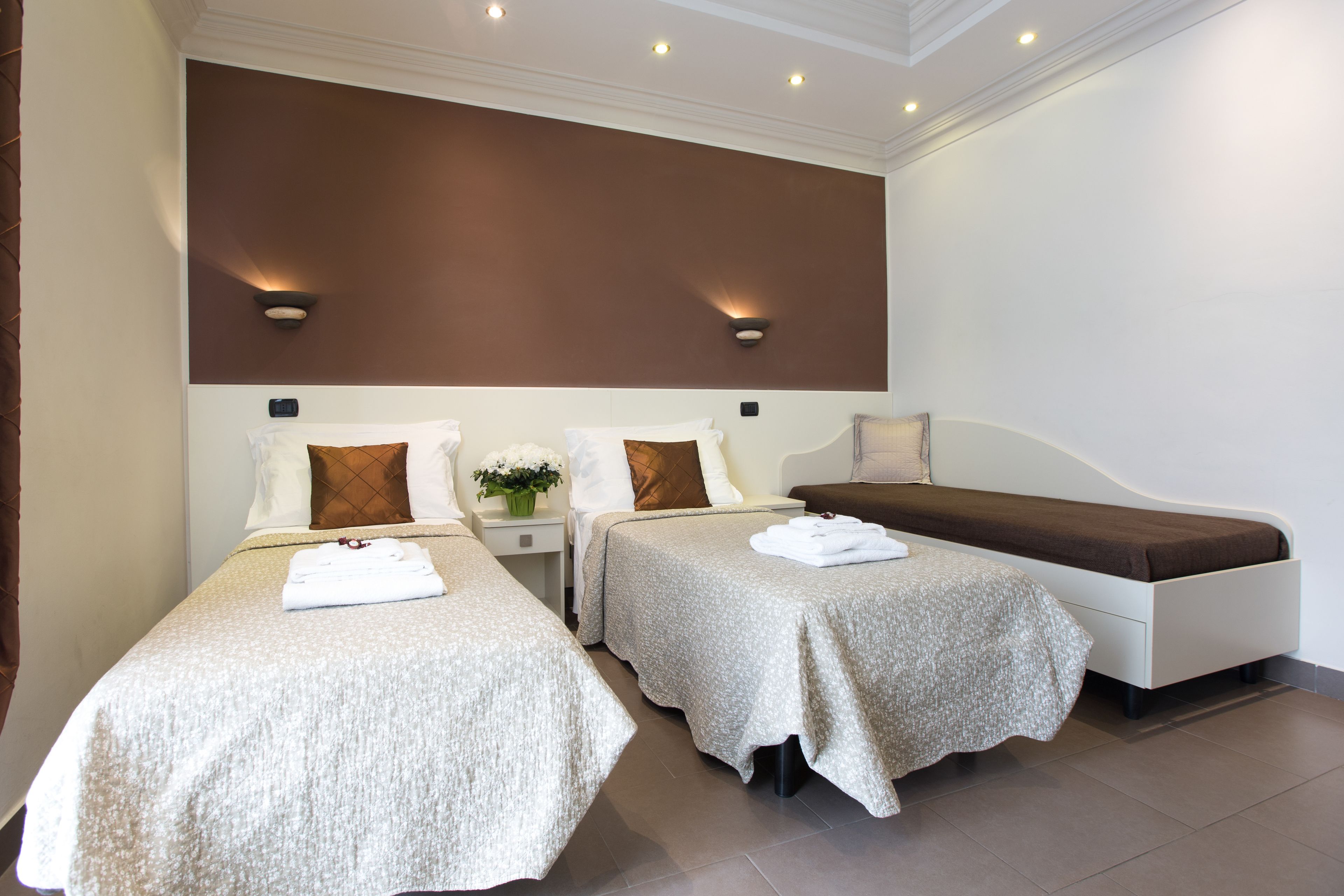 A hotel room with two single beds, a large window, and a wall-mounted light fixture.