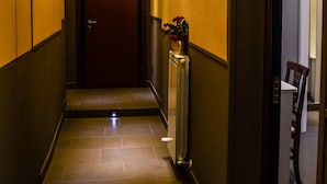 Een hotelgang met een donker houten deur, een radiator en een kleine plant.