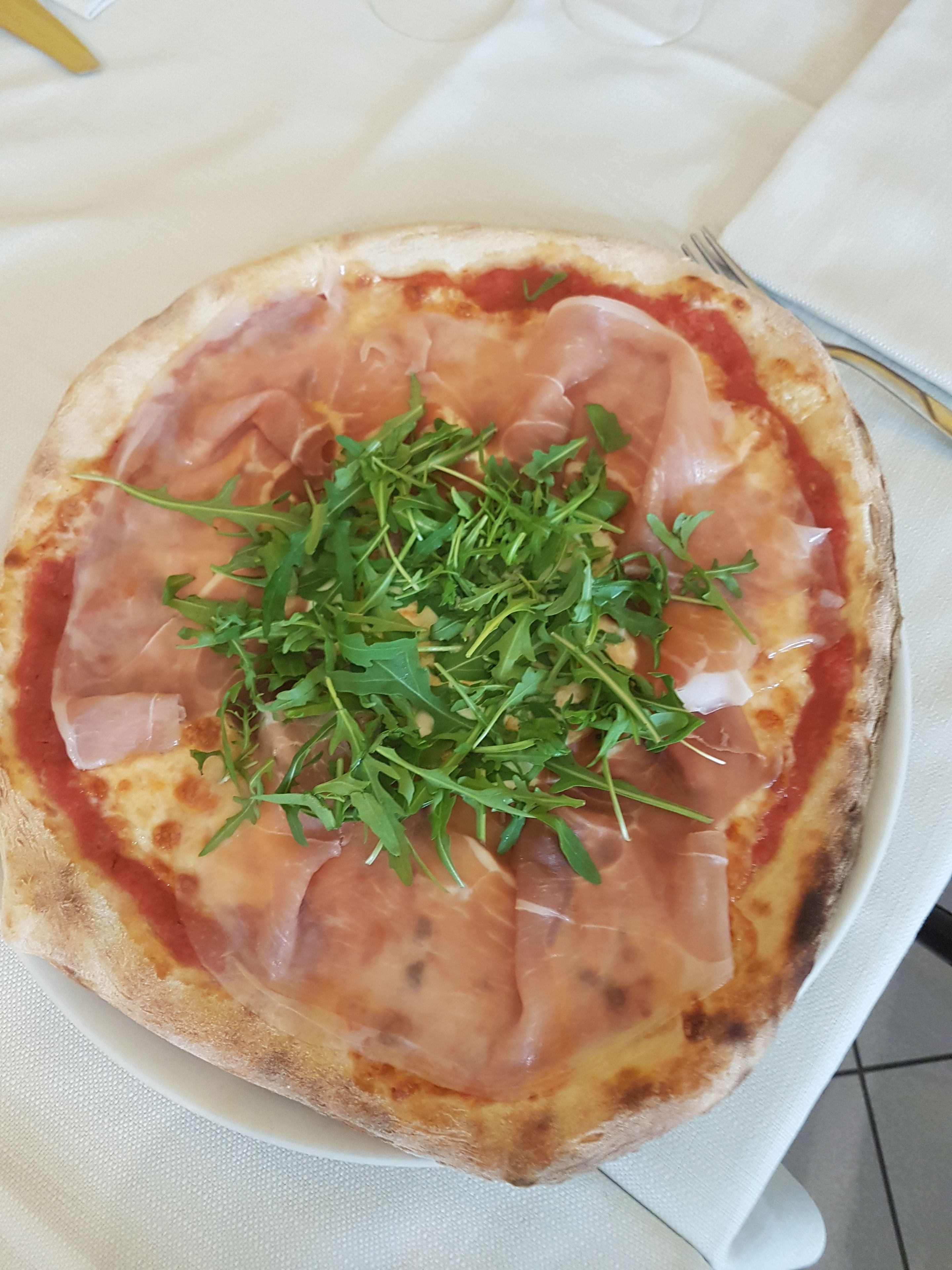 Pizza, jonka päällä on ilmakuivattua kinkkua ja rucolaa, tarjoiltuna valkoisella lautasella.