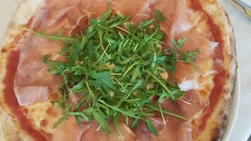 Pizza, jonka päällä on ilmakuivattua kinkkua ja rucolaa, tarjoiltuna valkoisella lautasella.