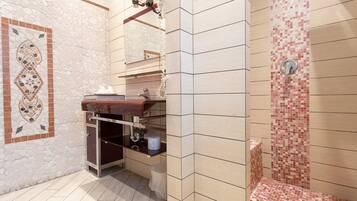 A bathroom with a stone mosaic wall, a wooden vanity, and a tiled shower area.