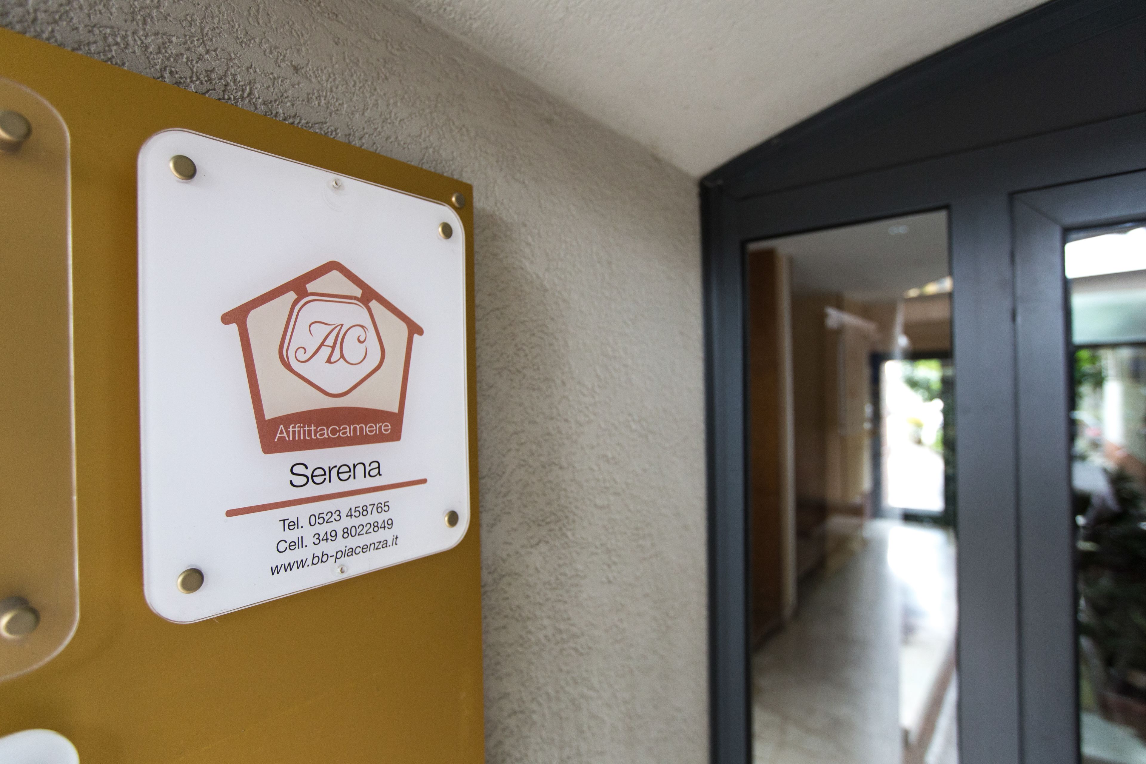 Une plaque portant le nom «Serena» et des coordonnées, fixée à un mur dont la surface est texturée.