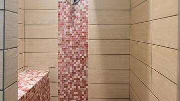 A shower with a tiled floor and walls, a showerhead, and a small shelf.