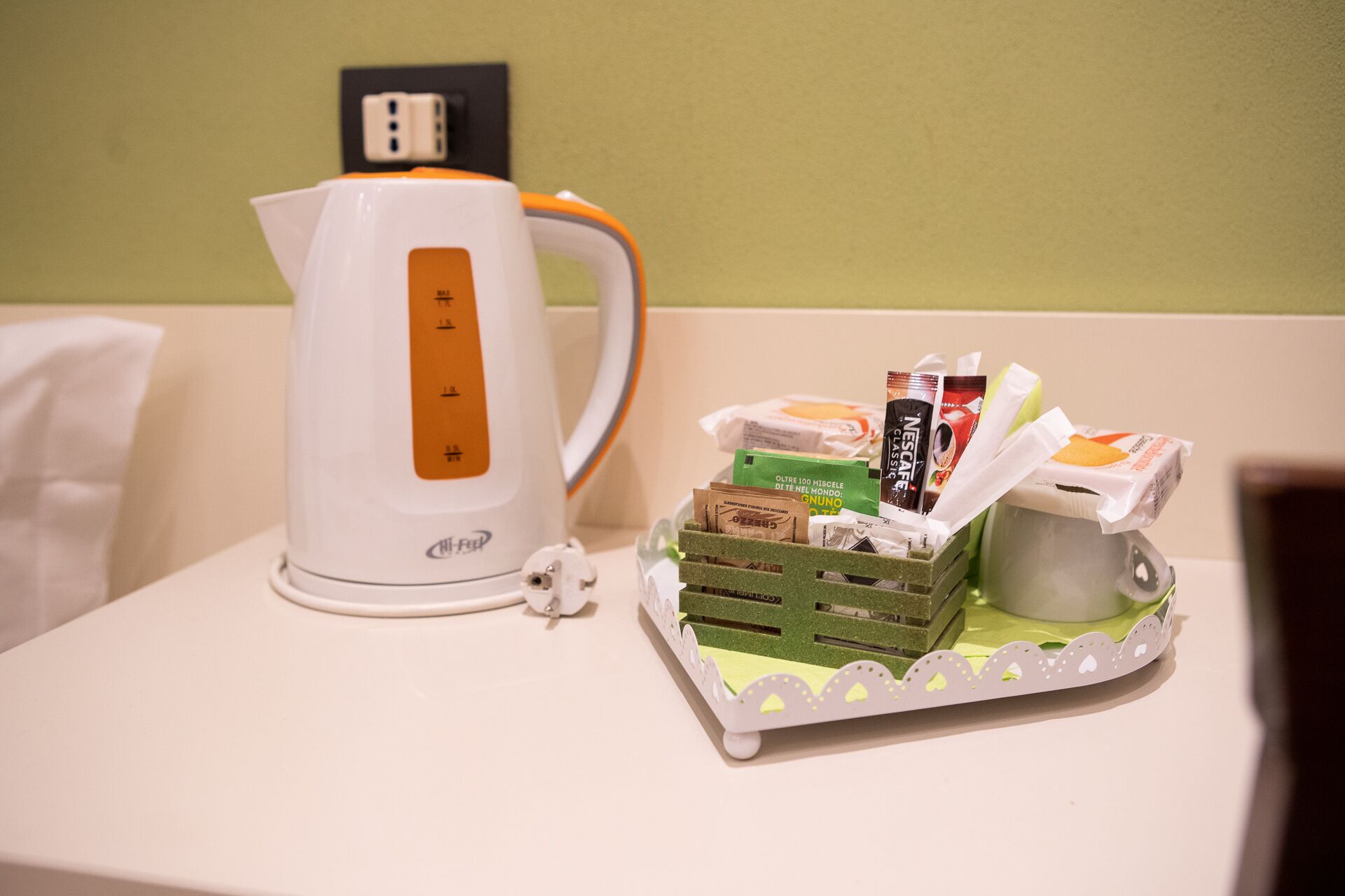 A white kettle and a tray with coffee pods and a Nespresso capsule on a table.