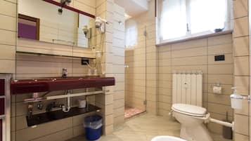 Et badeværelse med toilet, håndvask, spejl og bruser.
