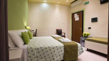 A hotel room with a bed, a chair, a small table with a vase of flowers, and a bedside table with a lamp.