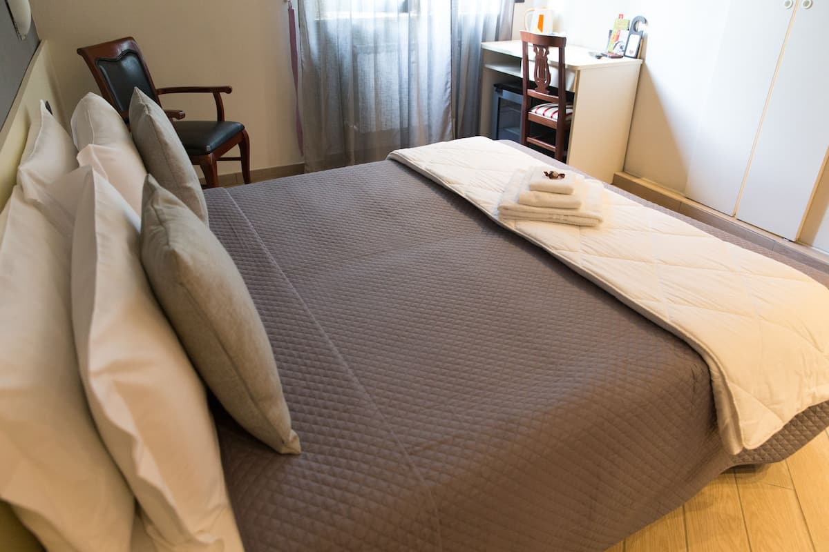A neatly made bed with a brown quilt, a chair, a desk, and a wardrobe in a hotel room.