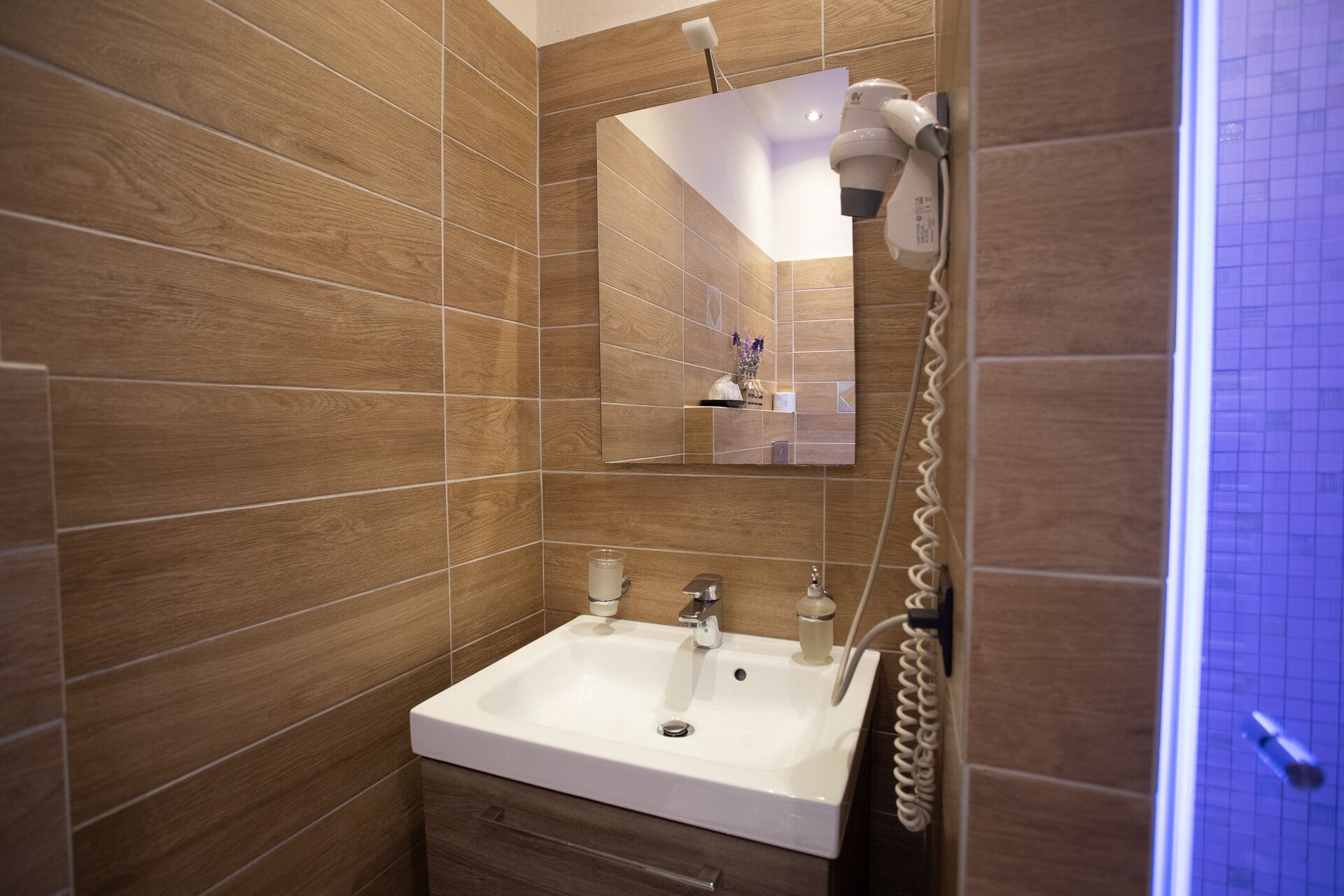 A modern bathroom with a white sink, a mirror, and a hairdryer mounted on the wall.