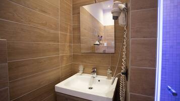 A modern bathroom with a white sink, a mirror, and a hairdryer mounted on the wall.
