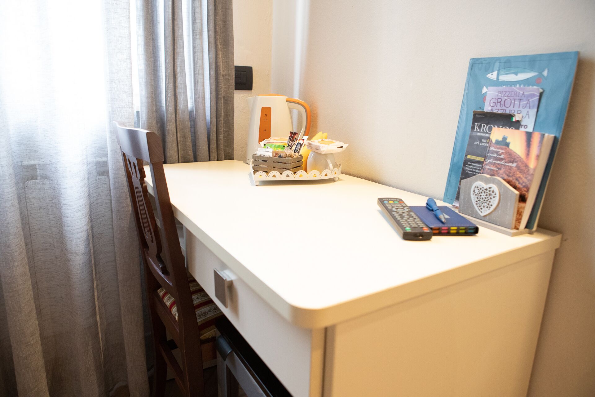 A small hotel room desk with a remote control, a pen, and a decorative item.