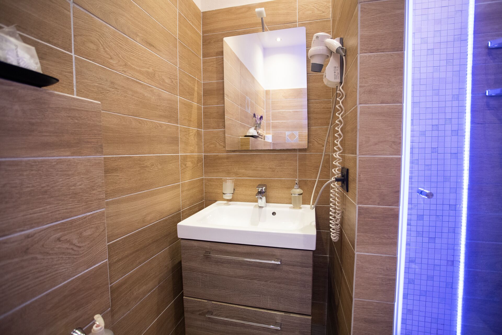 Ein modernes Badezimmer mit einem weißen Waschbecken, Holzwandverkleidung, einem Spiegel und einer Duschkabine.