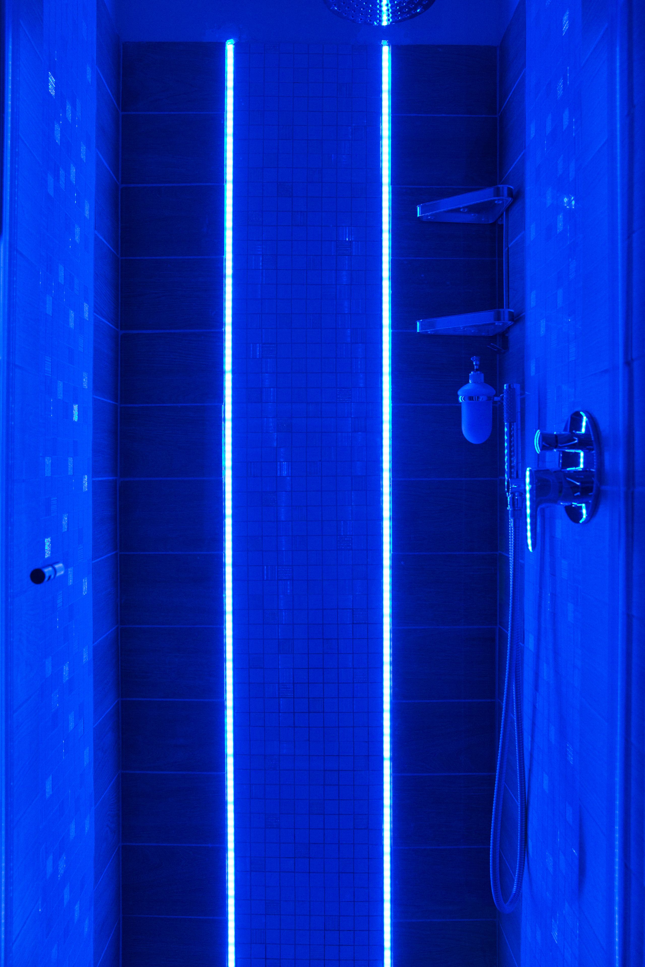 Ein modernes Badezimmer mit blauer LED-Beleuchtung, einer Duschkabine und einem WC.