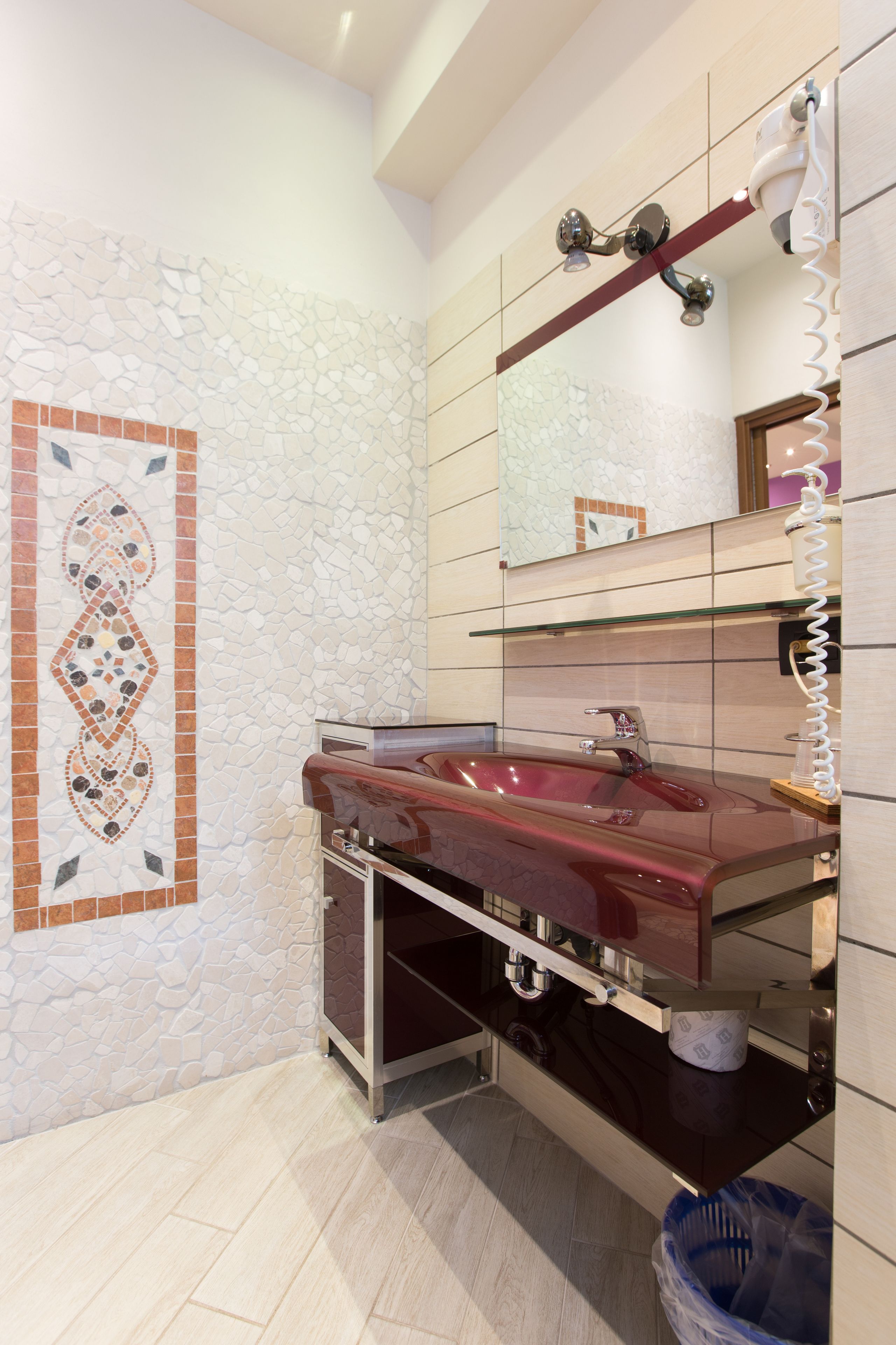 Un bagno con parete in mosaico di pietra, un lavandino rosso, uno specchio e un porta asciugamani.