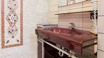 Un bagno con parete in mosaico di pietra, un lavandino rosso, uno specchio e un porta asciugamani.