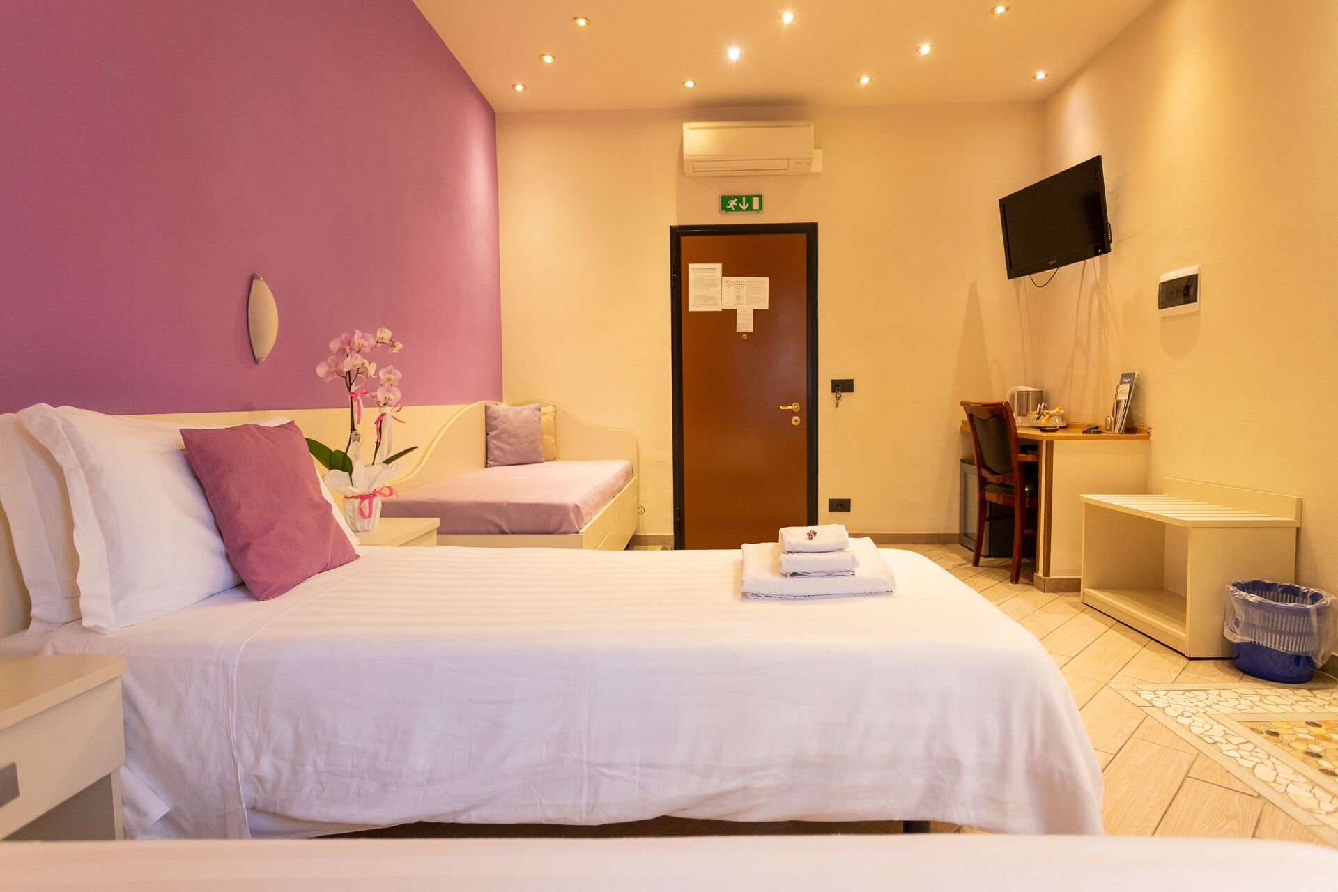 A hotel room with a bed, a desk, a chair, a TV, and a bathroom.