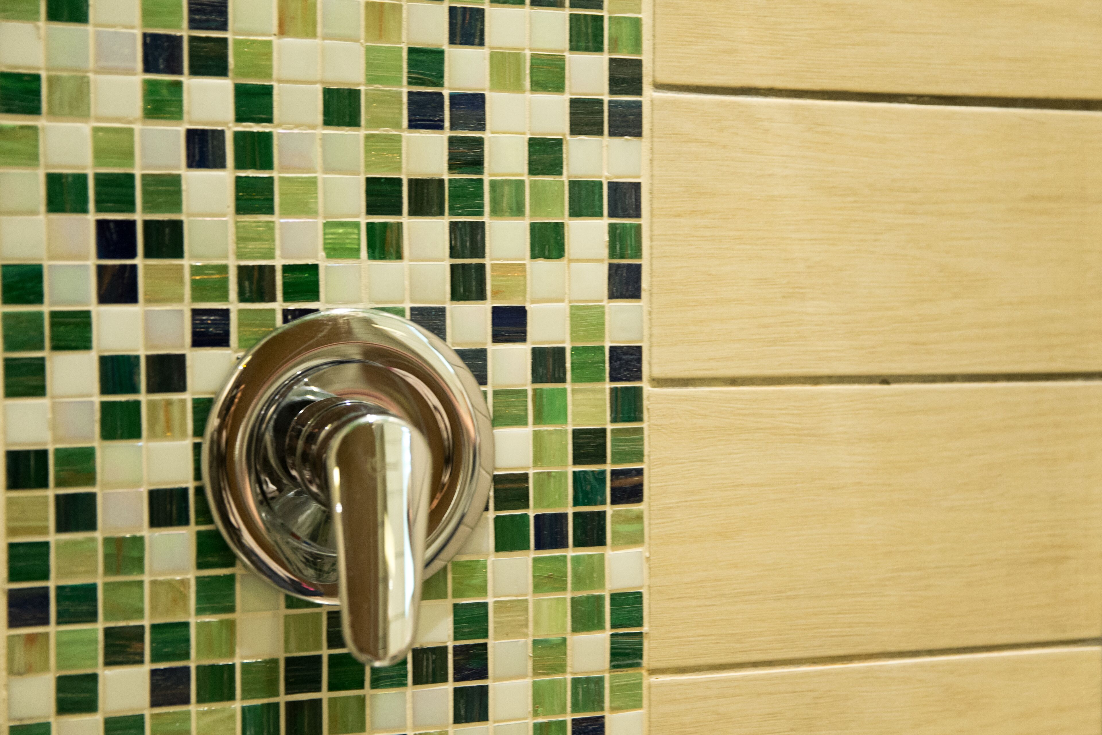 A bathroom with a tiled wall featuring a green and white mosaic pattern and a chrome faucet.