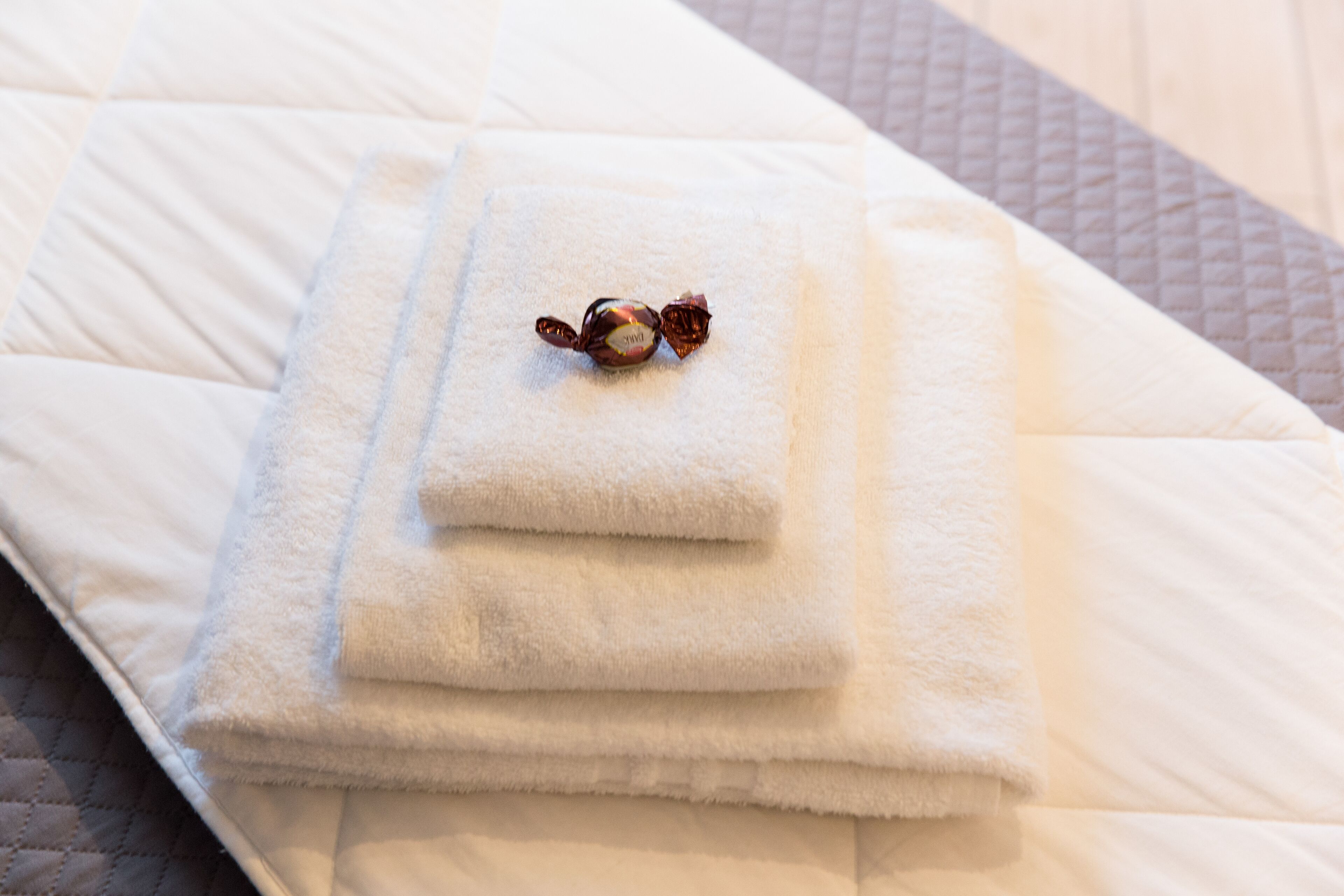 A neatly folded white towel on a bed with a quilted cover.