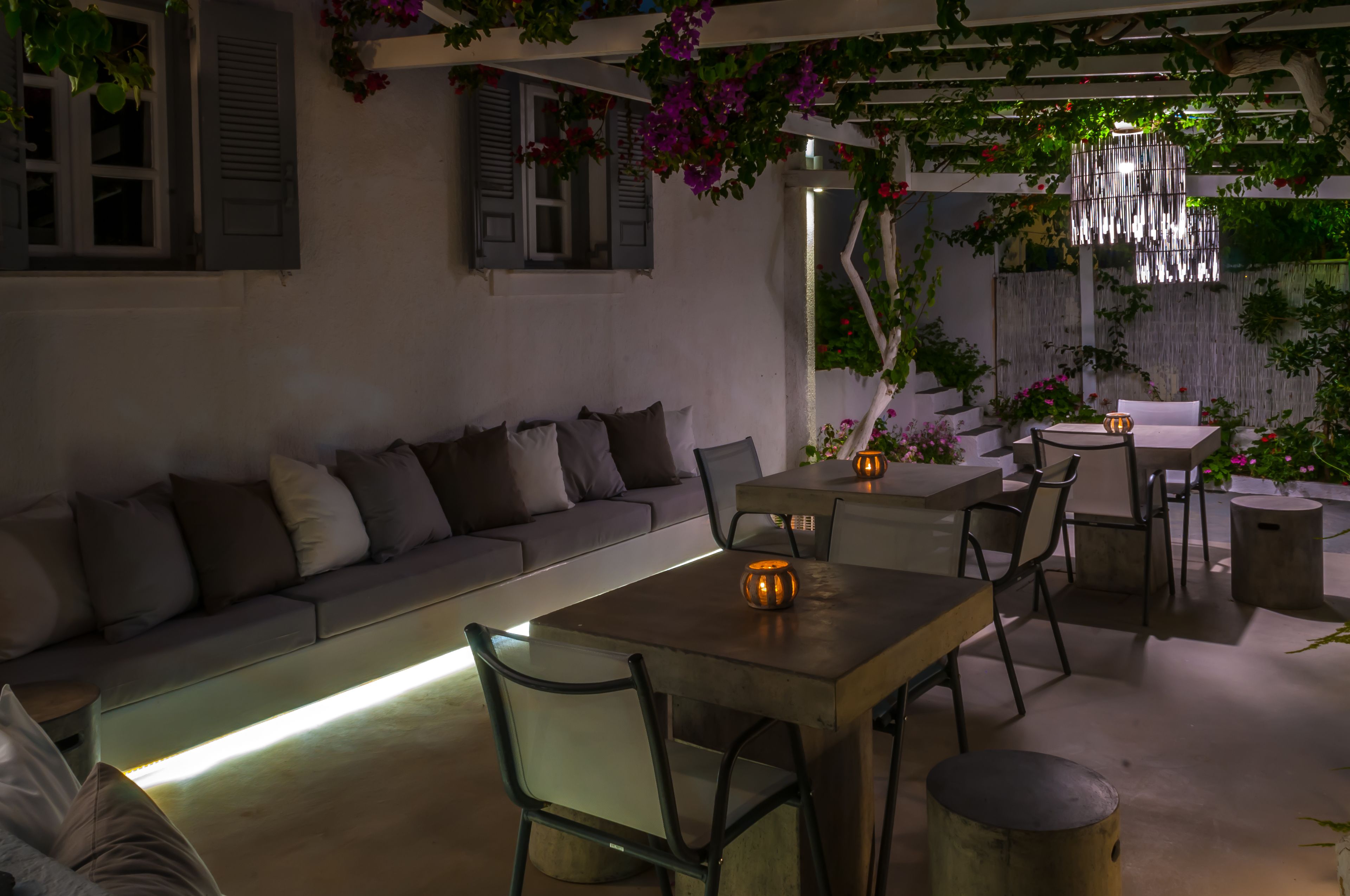 Un área de estar al aire libre con un sofá, una mesa y sillas, rodeada de plantas y flores.