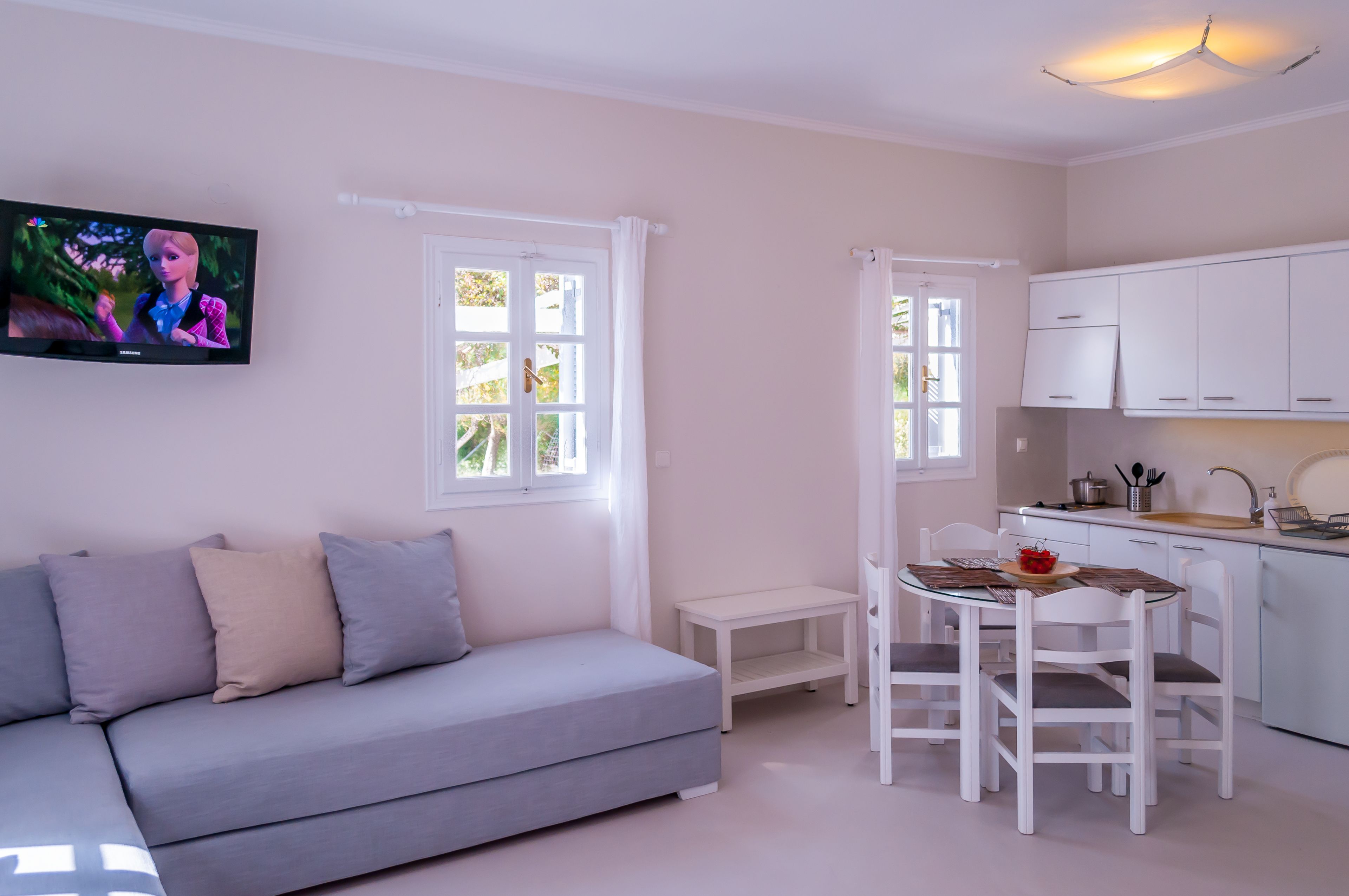 Una sala de estar moderna con un sofá gris, una mesita blanca y un comedor con sillas y una mesa blancos.