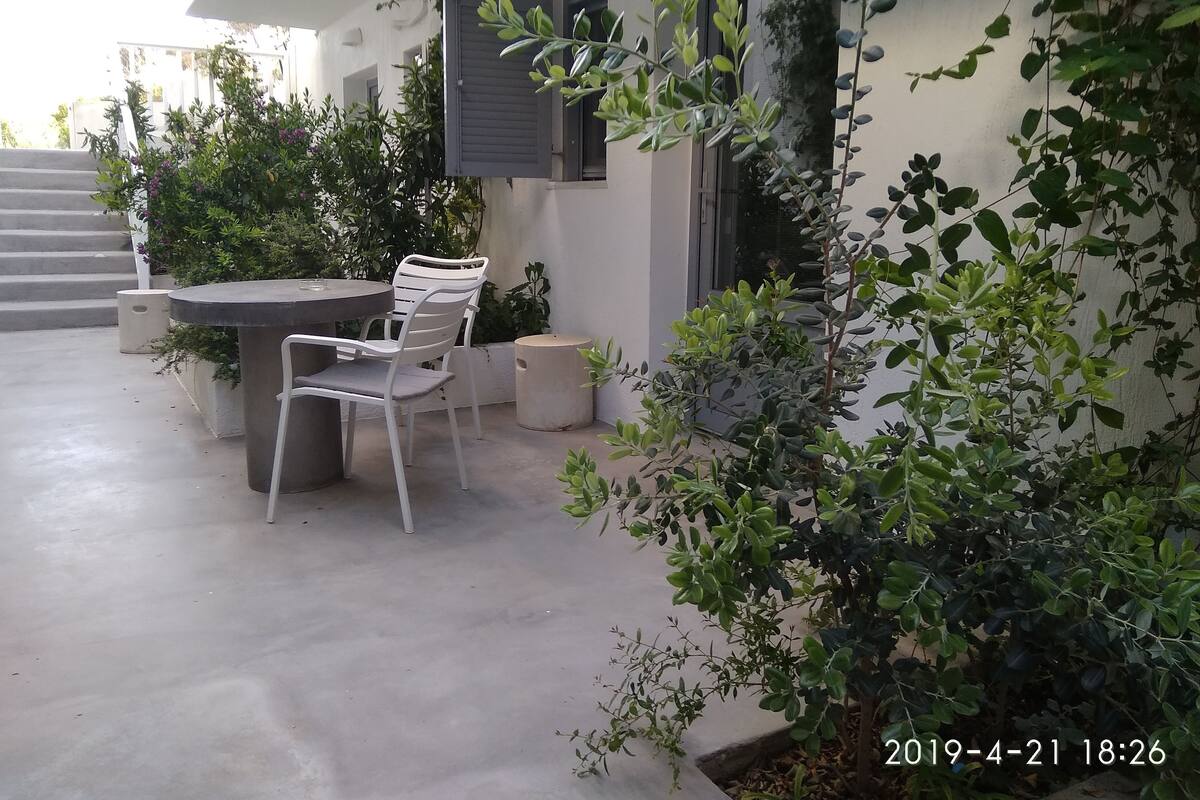 An outdoor patio with a round table and two chairs, surrounded by potted plants and a staircase leading to an upper level.