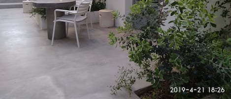 Un patio al aire libre con una mesa redonda y dos sillas, rodeado de plantas en macetas y una escalera que lleva a un nivel superior.