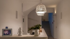 A modern interior with a central island featuring a television, a white lantern, and a potted plant. A staircase is visible in the background. - Milos Bay Suites (Milos)