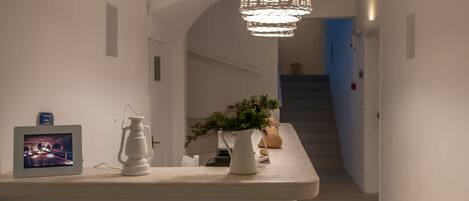 Un intérieur moderne avec un îlot central agrémenté d’un téléviseur, d’une lanterne blanche et d’une plante en pot. Un escalier est visible au fond.