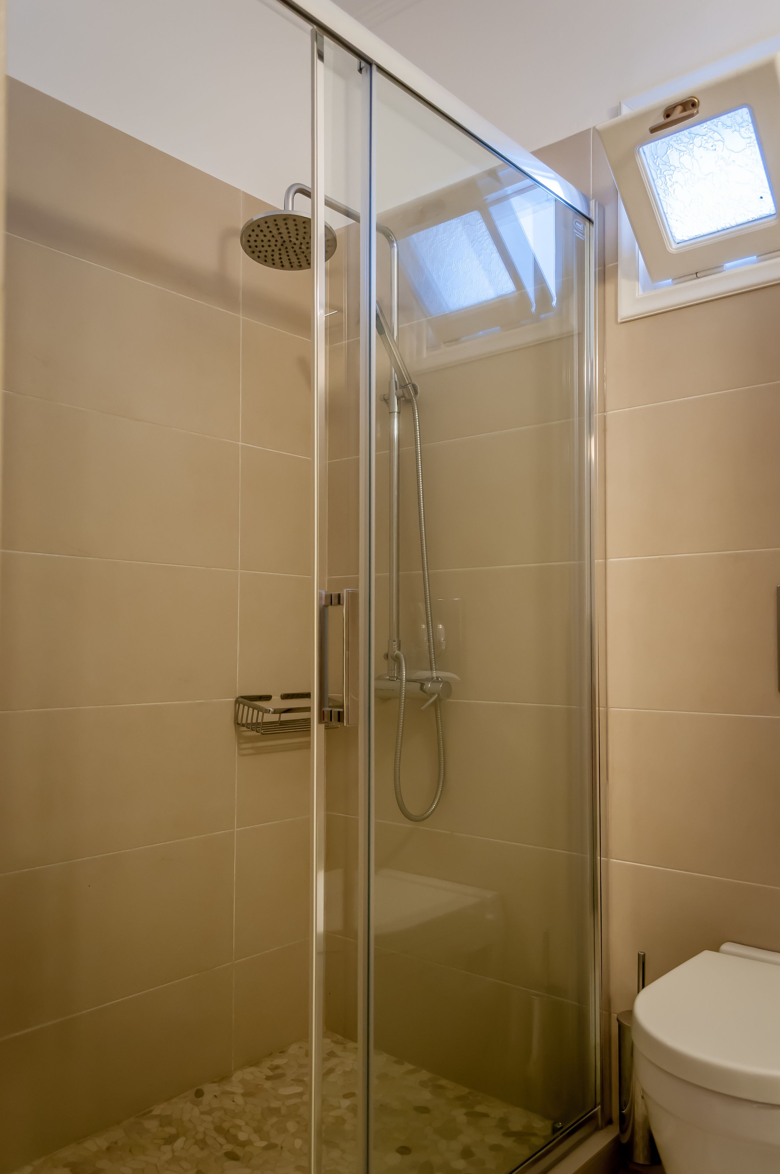 A glass-enclosed shower with a handheld showerhead and a handheld faucet.