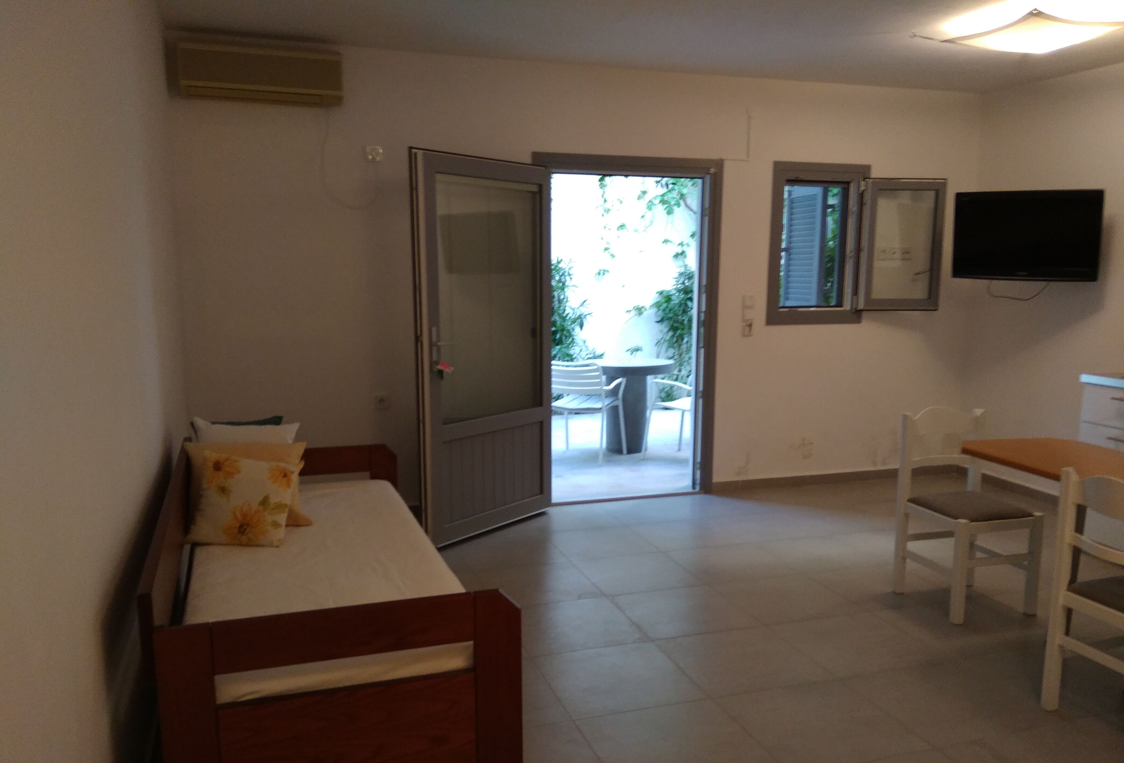 Una habitación con cama, escritorio, silla, televisión y puerta que da a un espacio exterior.