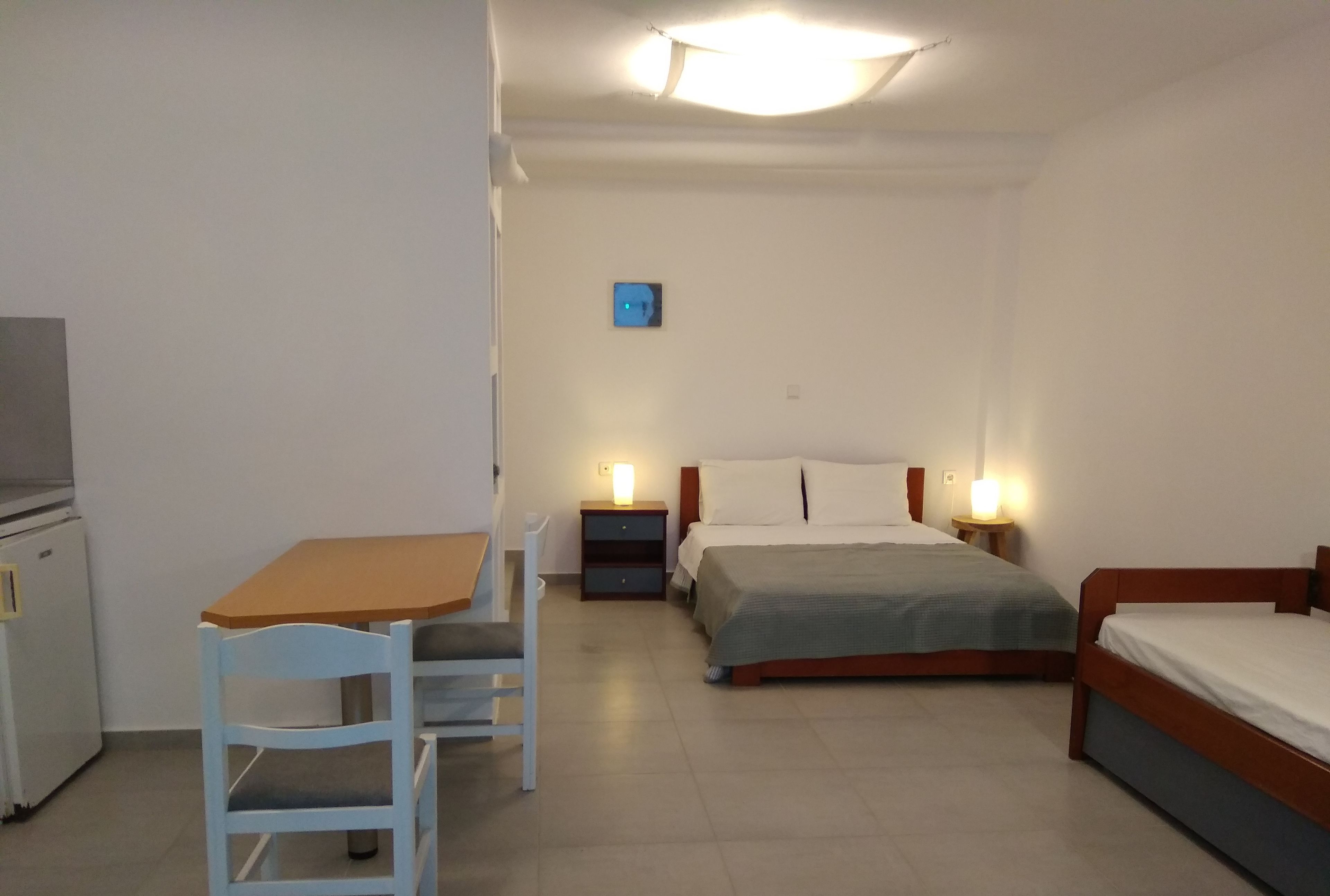 A bedroom with a single bed, a bedside table with a lamp, a small bedside table with a lamp, a chair, and a desk with a chair.