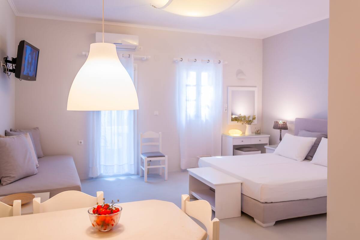 A modern bedroom with a bed, bedside table, chair, and a dining area with a table and chairs.