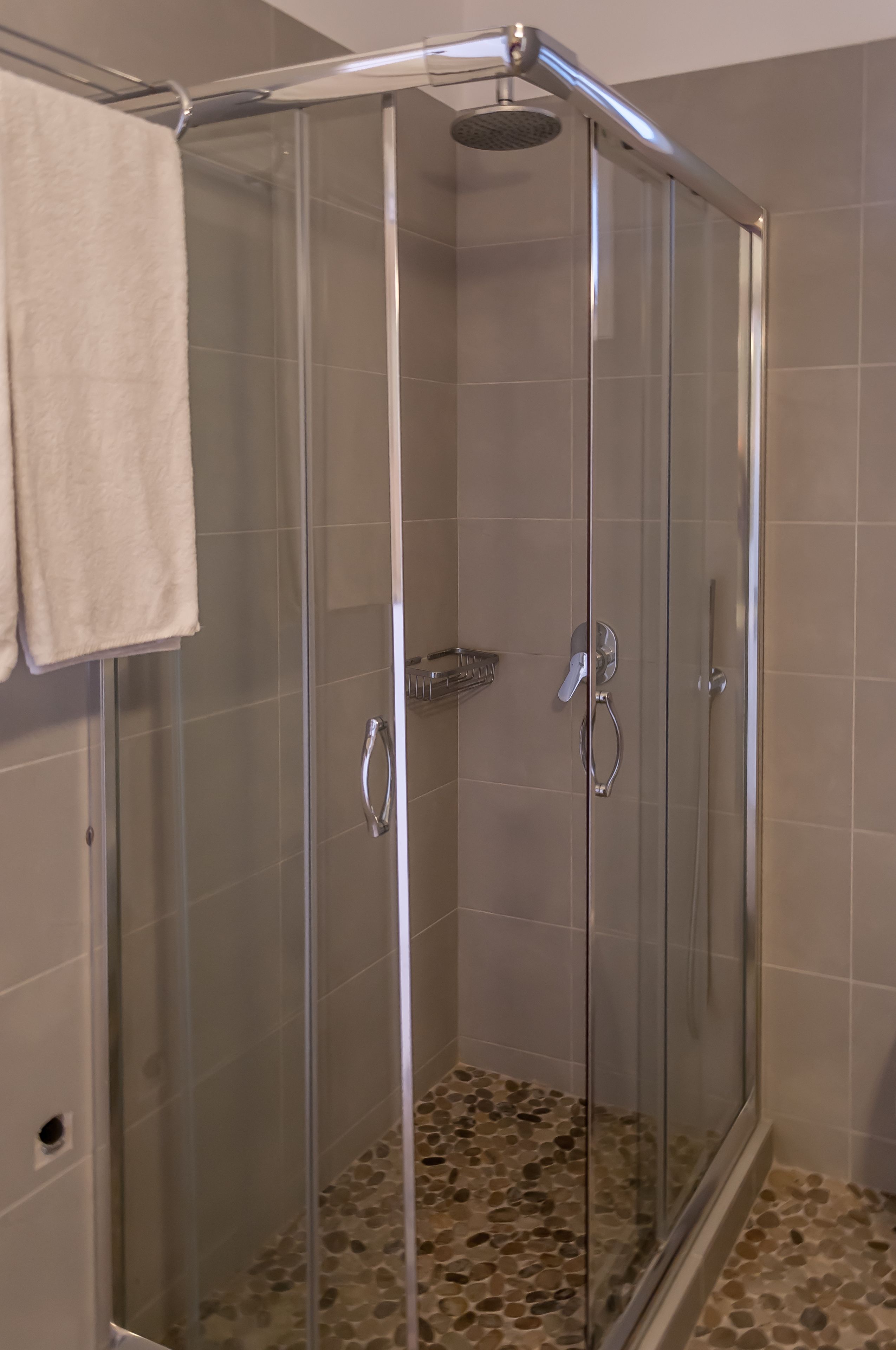 A glass-enclosed shower with a handheld showerhead, a towel rack, and a pebble-patterned floor.