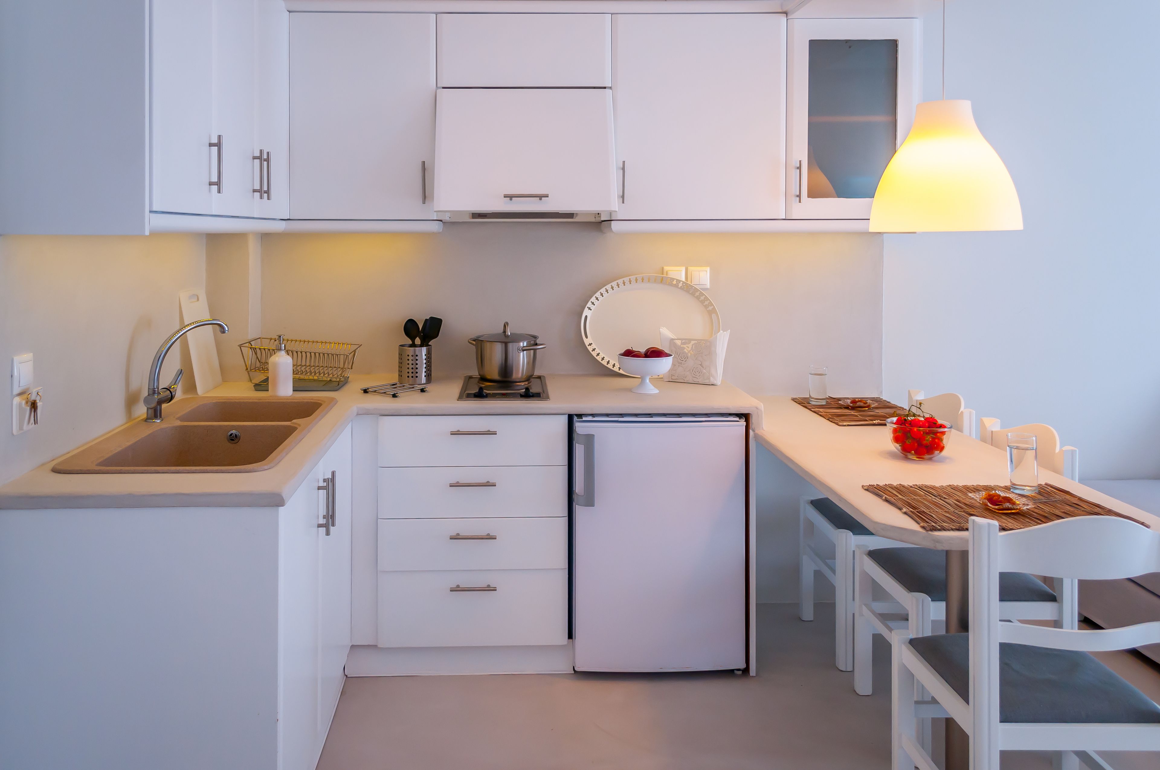 A compact kitchen with white cabinets, a sink, a small refrigerator, and a dining area with a table and chairs.