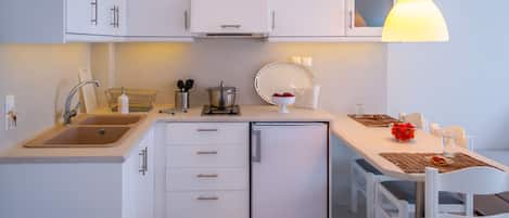 A compact kitchen with white cabinets, a sink, a small refrigerator, and a dining area with a table and chairs.
