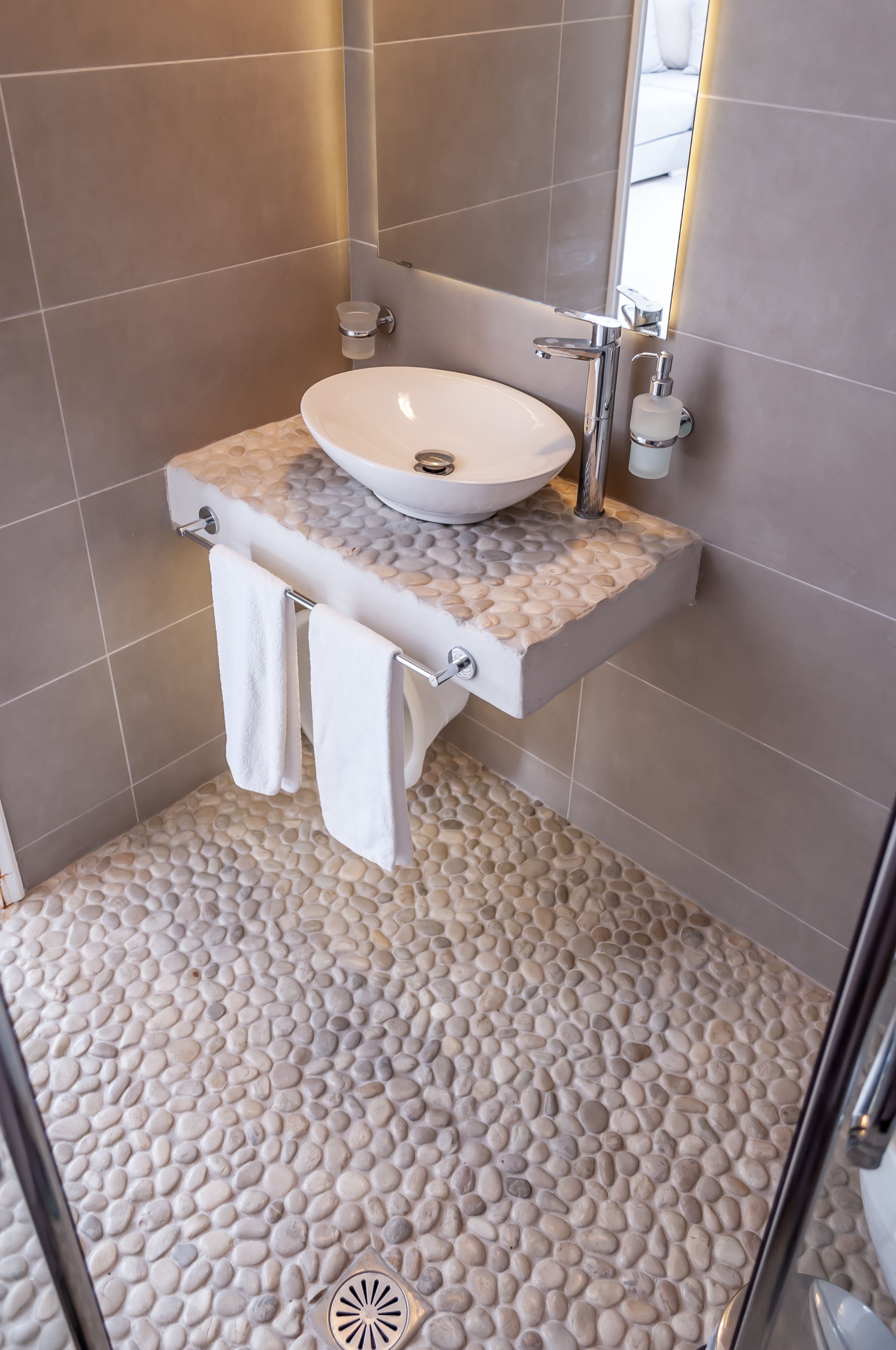Un baño con piso de diseño de guijarros, un lavamanos blanco con encimera de mármol y un espejo sobre el lavamanos.