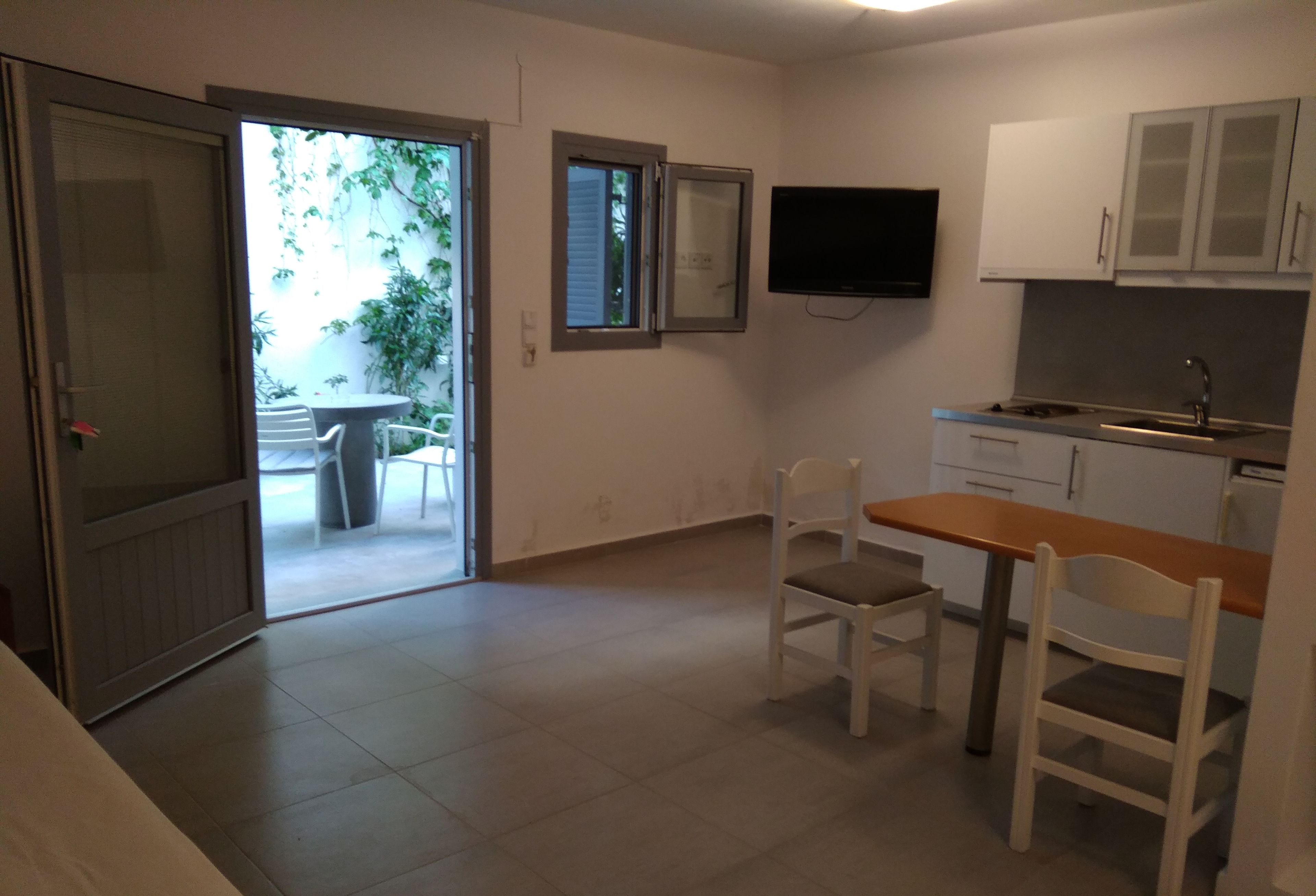 Una cucina compatta con angolo ristoro, una TV montata sopra il bancone e una porta vetrata scorrevole che dà su un patio esterno con sedie e piante.