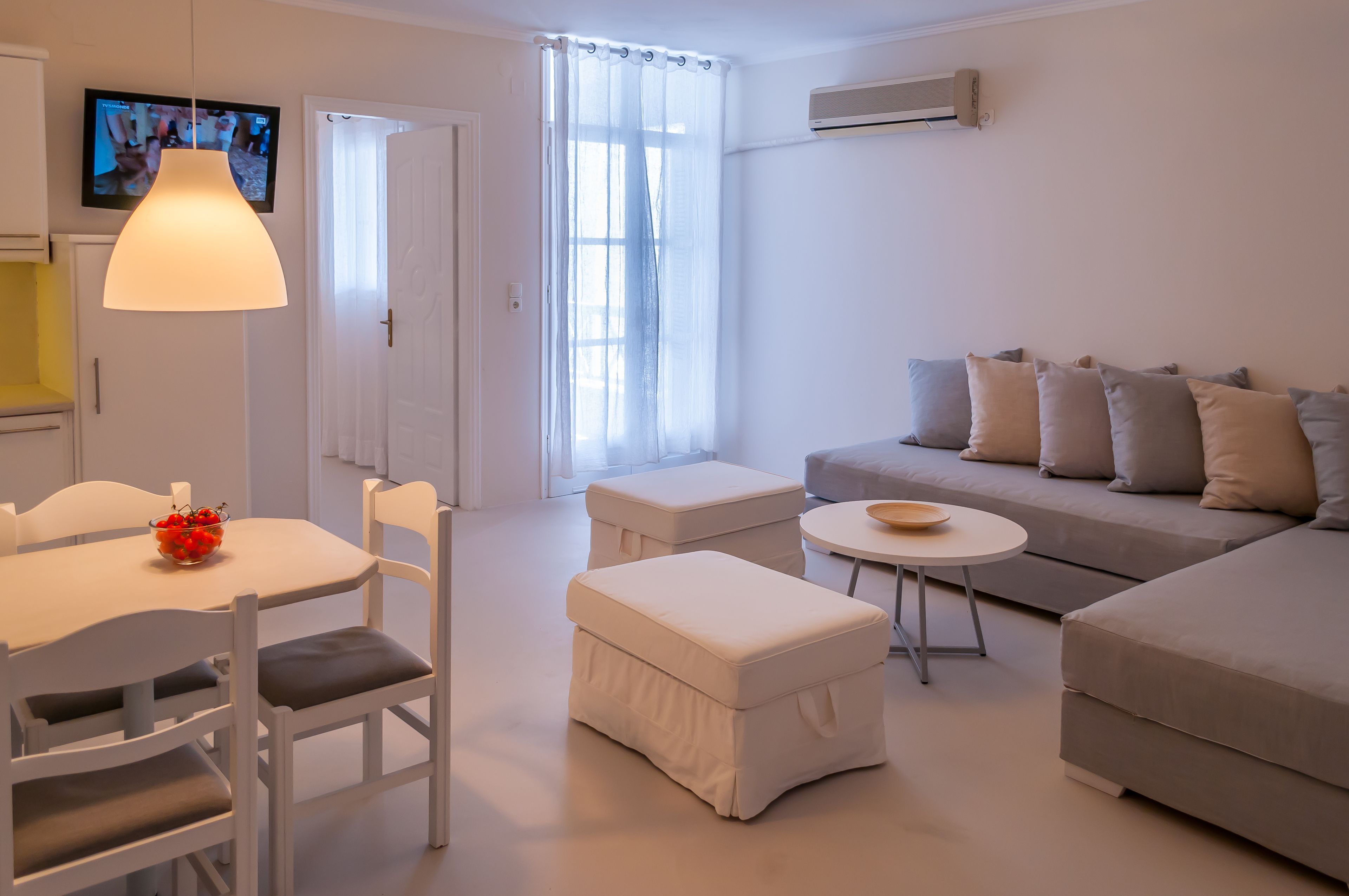 A modern living room with a sofa, ottomans, a dining table with chairs, and a TV mounted on the wall.