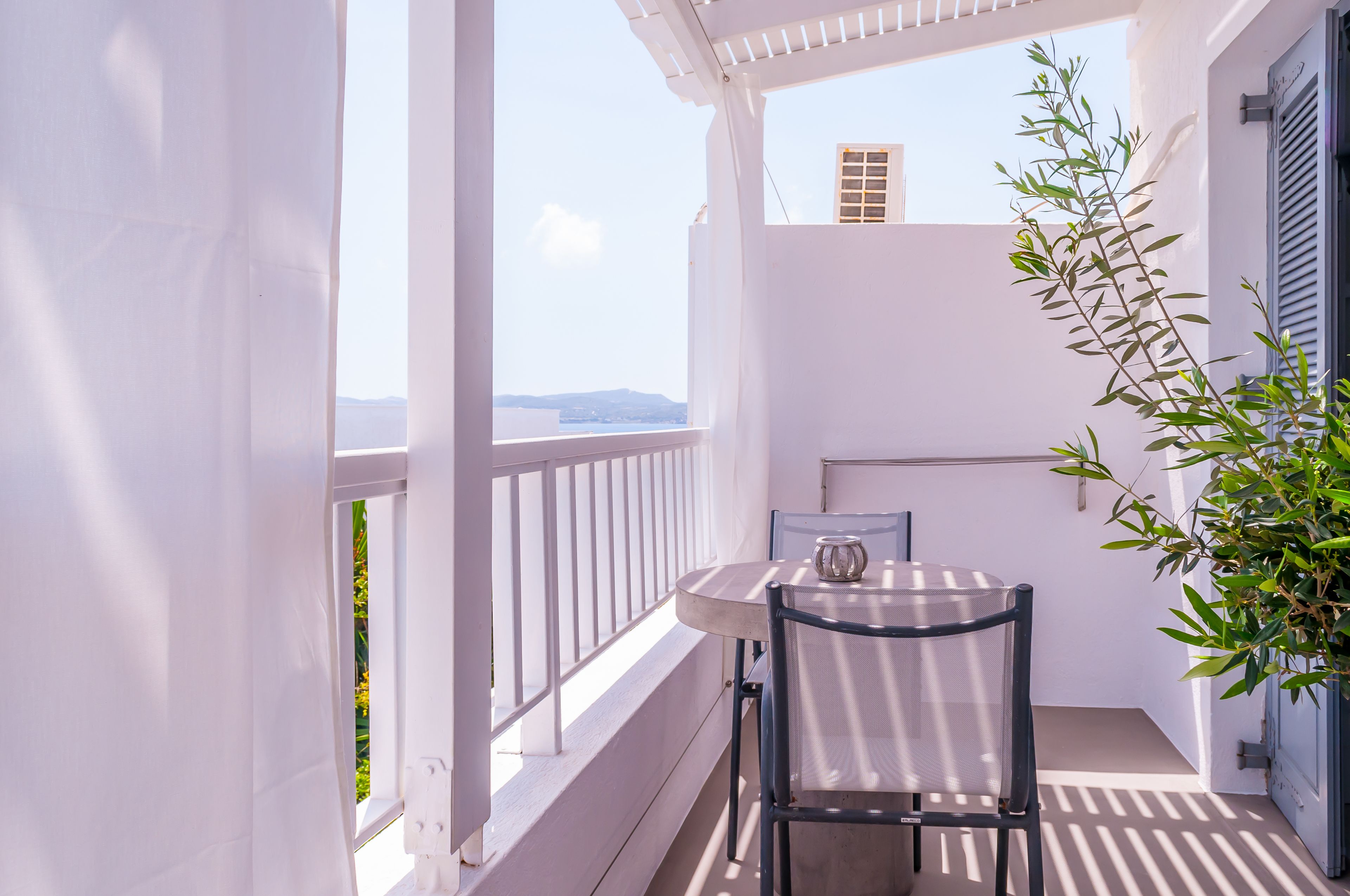 A balcony with a table and chair, a potted plant, and a view of the sea.