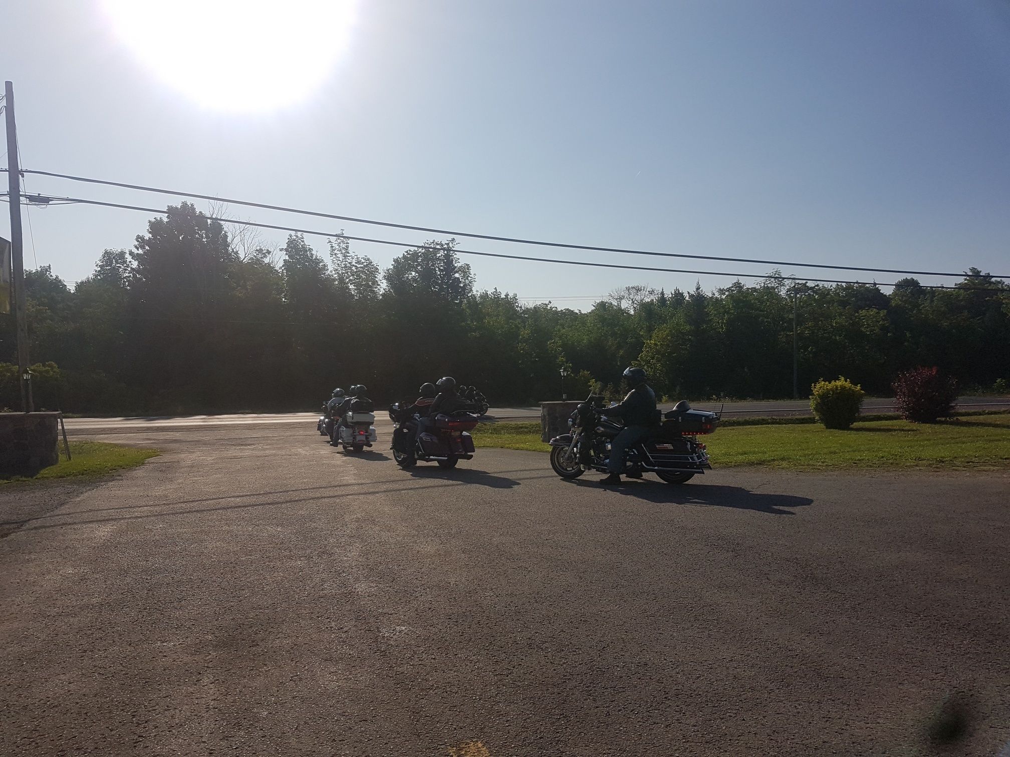 Un groupe de motocyclistes circulant sur une route asphaltée, avec des arbres et de la végétation en arrière-plan.