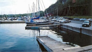 Un puerto deportivo con barcos amarrados, un muelle de madera y un aparcamiento con coches.