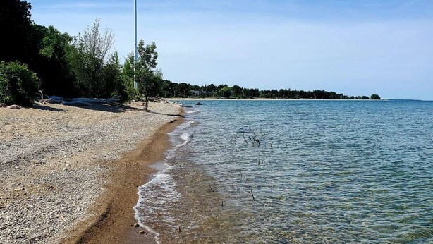 Una playa con agua cristalina, una bandera y una costa lejana.