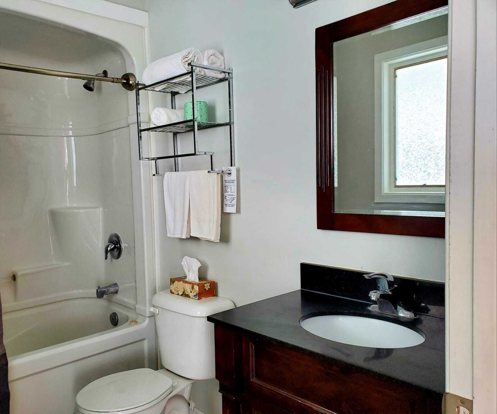 Un baño con bañera, inodoro y lavabo. Hay toallas y artículos de aseo en un estante.
