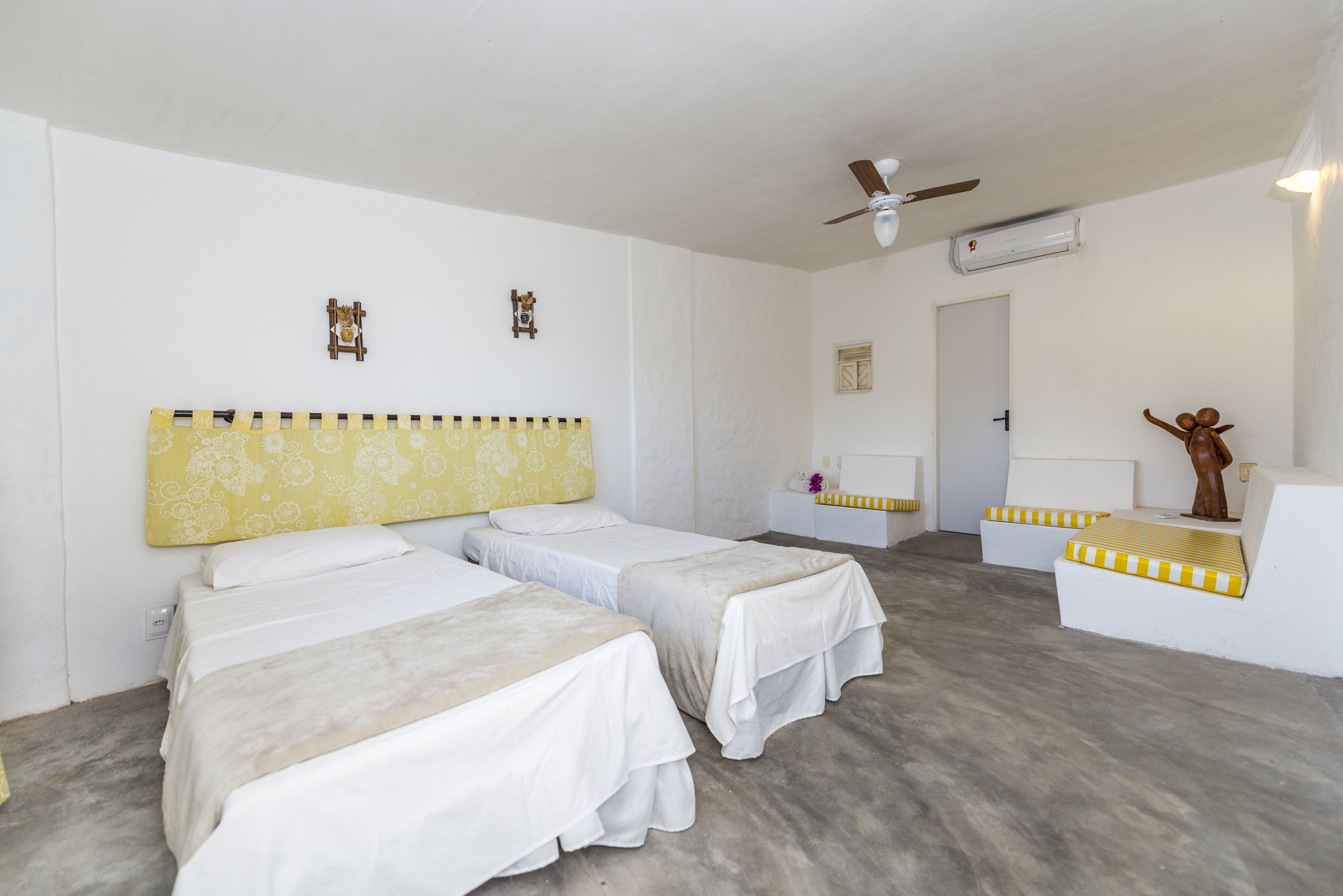 A hotel room with two single beds, a ceiling fan, an air conditioning unit, and a small statue on a pedestal.