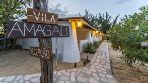 Un senyal de fusta amb les indicacions 'VILA AMAGALI' i 'RECEPCIÓ', que guia cap a un edifici amb un camí de pedra i plantes.