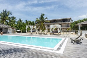 A pool area with wooden decking, lounge chairs, and a thatched-roof structure. - Amagali Pousada (Galinhos)