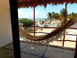 A hammock on a balcony overlooking a beach with a pool and palm trees. - Amagali Pousada (Galinhos)