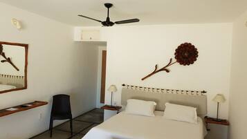 A hotel room with a bed, a chair, a desk, a ceiling fan, and a wall decoration.