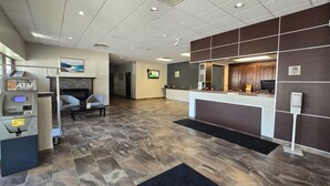 A reception area with a reception desk, a fireplace, an ATM, and a television screen. - Rodeway Inn (Sudbury)