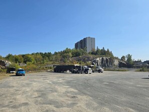 A parking lot with a large building on a hill, a blue car, and two trucks.