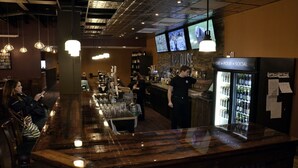 A bar area with a counter, multiple hanging lights, a refrigerator with beverages, and a television screen displaying sports. - Rodeway Inn (Sudbury)